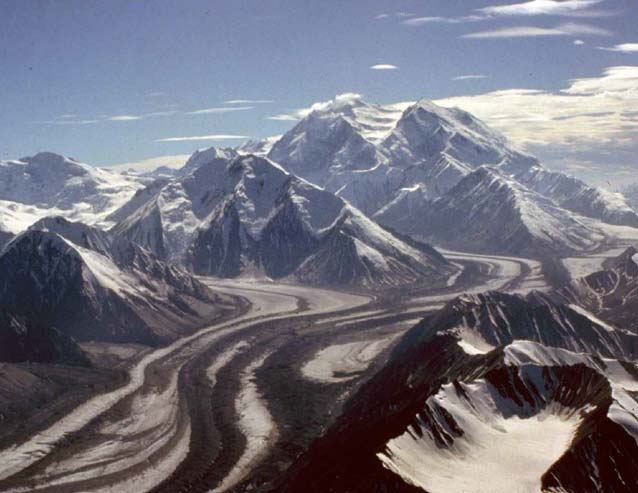 aerial view of a vast white mountain with numerous glaciers and smaller mountains