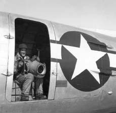Man sitting with a giant camera in an open door of an aluminum plane