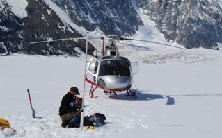 man kneeling in snow, near a helicopter