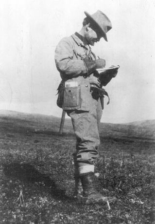 black and white image of a man writing in a notebook while standing on a hillside