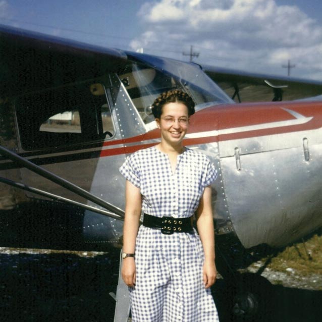woman in a dress standing next to a 1940s-era plane