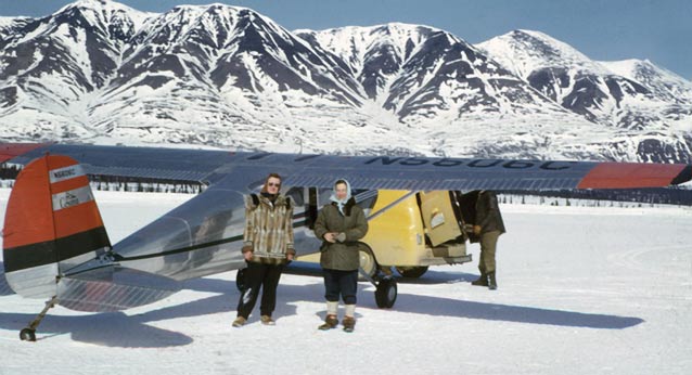 Two women standing near a small plane that is parked on a frozen lake or snowy landing field