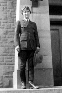 woman in ranger uniform standing by a wall holding her hat