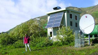 woman standing in front of a small white building with big solar panels on it