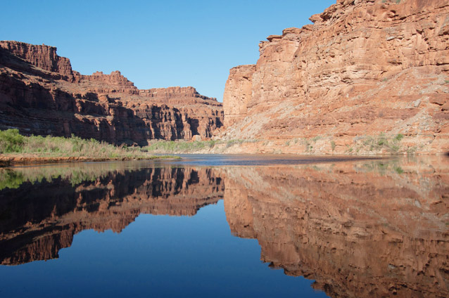 The Colorado River flowing through a canyon and reflecting the reddish canyon walls and blue sky