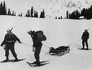 B&W; soldiers on snowshoes tow sled with person in it