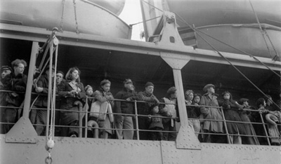 A crowd stands at the railing of a ship, looking off into the distance.