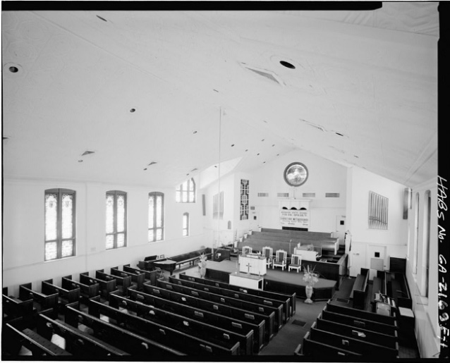 A high angle view of the pulpit, organ, and pews within the white-walled interior of a church.