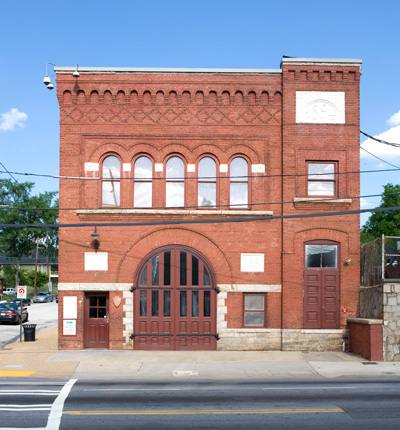 The fire station is a rectangular, red brick building with arched doors, windows, and brickwork.