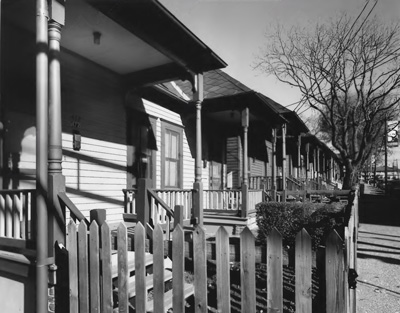 Wooden fencing surrounds the small yards and porches in front of a row of shotgun homes.