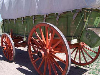Side view of a green-colored covered wagon with red wheels. 