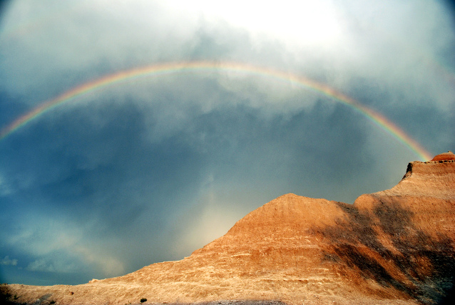 A rainbow against a cloudy sky over mountains at Badlands National Park
