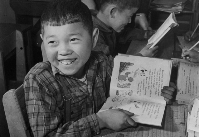 Historic photo of a third grade boy holding a book at the Manzanar War Relocation Center