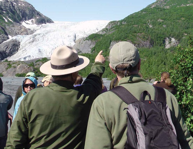 a park ranger next to a visitor points up the mountain with a glacier in the background