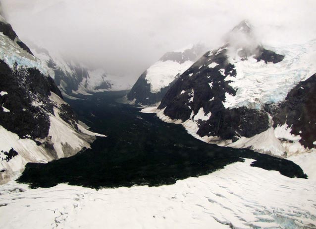 a rock debris field on a large glacier surrounded by snowy mountains