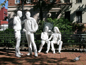 White statues of people in a park, two standing and two sitting on a park bench