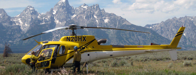 Two pilots and a park service helicopter in a field with mountains in the background.