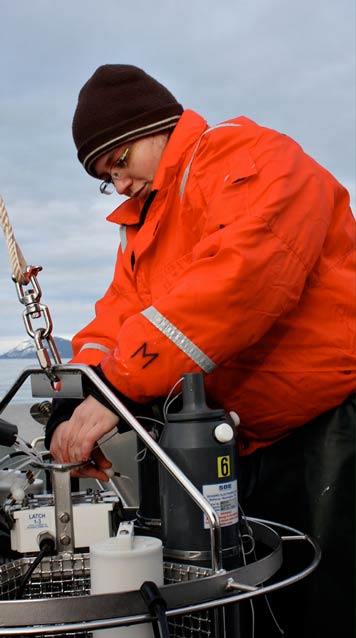A woman in a bright orange jacket adjusting some kind of scientific equipment