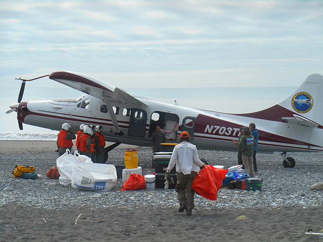 people loading plastic bags into a small plane on a rocky beach