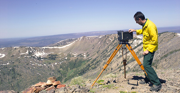 Ian Grob adjusts an Osborne photo recording transit looking out over mountain and valley.