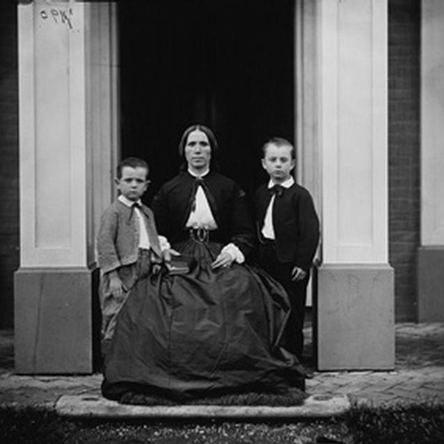 Photograph of two children with their mother outside their home