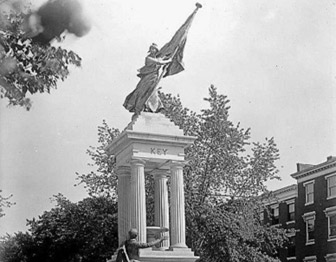 Black & white photograph of stone memorial with female figure holding flag. Key is craved in stone.