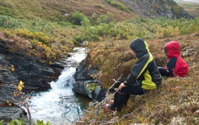 Two children sit at the edge of a waterfall