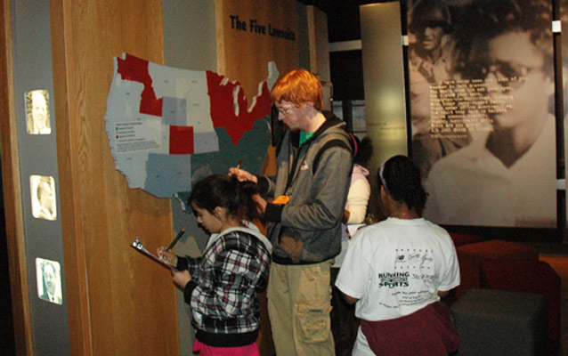 A teacher and students research answers at The Five Lawsuits exhibit.