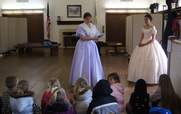 Volunteers in period clothing instructing elementary students about leisure pasttimes of the soldiers.