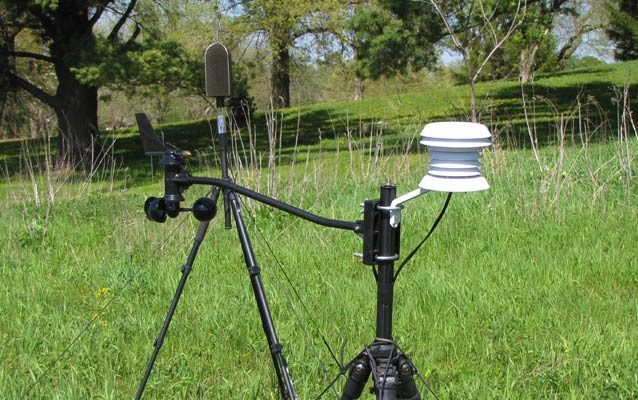 A portable weather station and sound monitoring instrument set up in a field.