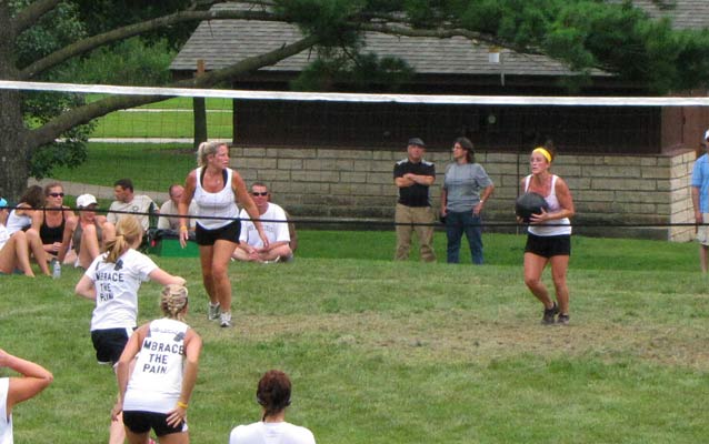 Teams of women pass a medicine ball over a volleyball net.