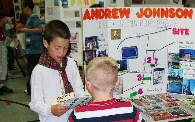 A third grade boy explains his national park display to a classmate.