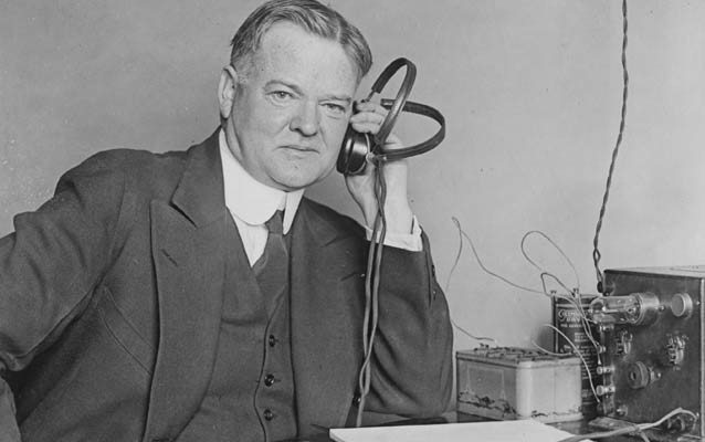 Black and white photo of Herbert Hoover in front of a radio set.