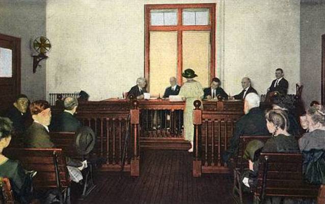 People seated in a courtroom setting with three judges at front with other officials (Photochrom image).