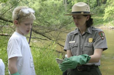 Ranger and boy with blonde hair and goggles standing. Ranger is holding a vile and wearing gloves.
