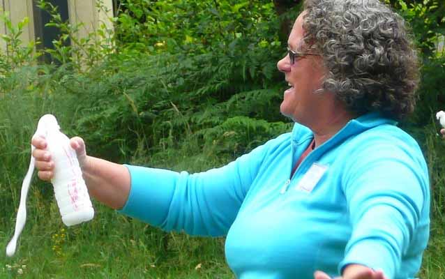A teacher holds a plastic bottle with white bubbles streaming from the top, demonstrating the Soda Bottle Volcano.