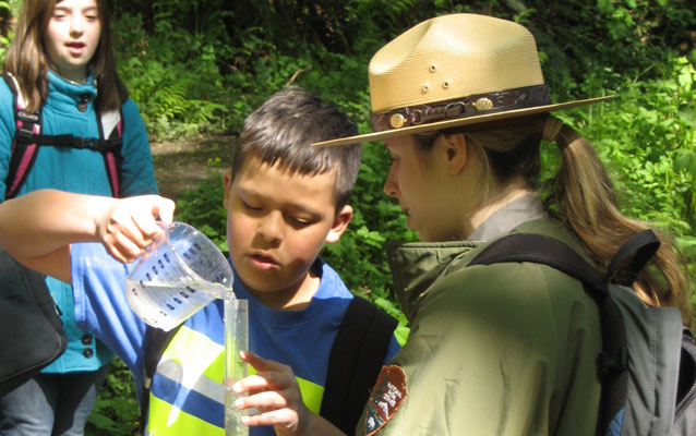 A ranger assists a student demonstrating how to measure water turbidity.