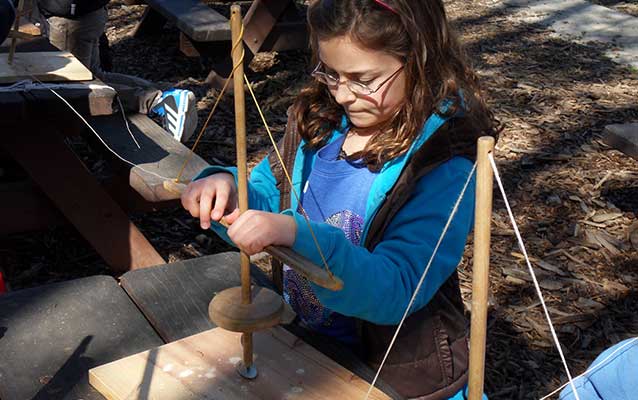 A student uses a hand drill to make a shell necklace