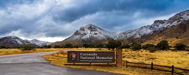 Snow covered mountains with park entrance sign in foreground sign.