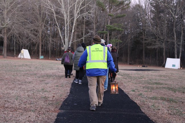 Volunteer with reflective vest walks down a path with a lantern