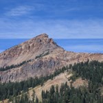 Brokeoff Mountain at Lassen Volcanic National Park a pointed mountain peak rises into the blue horizon, a green forest greats a linear designation of the subalpine region about 1/3 up the mountain
