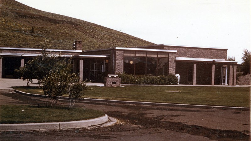 a colorized photo of a brick building with a large green lawn in front