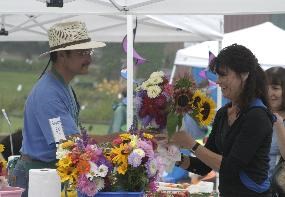 A man in a straw hat stands under a white tent selling flowers.