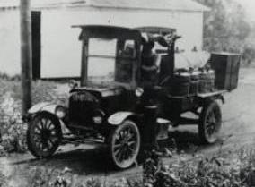 Black and white photo of a model T car as a delivery truck stacked with goods.