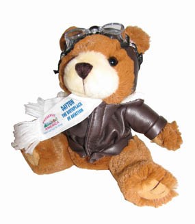A stuffed teddy bear wearing a brown jacket and goggles on his head and a white scarf