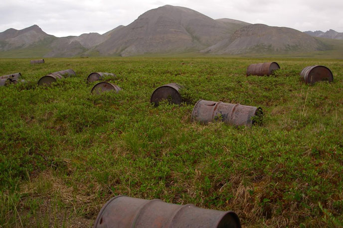 rusty barrels in a tree-less field, mountains in the distance