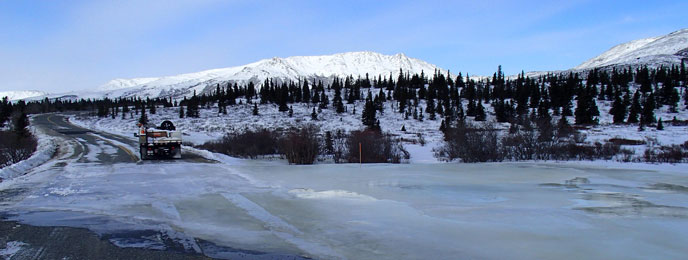 image of mountains, forest, and thick ice frozen across a paved road
