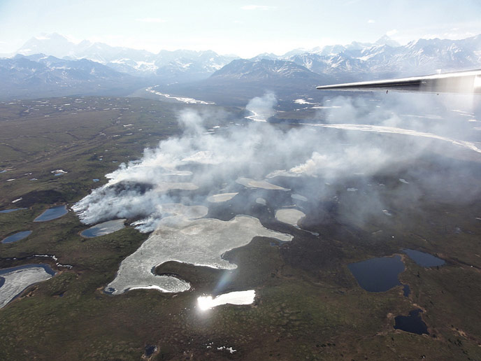 aerial image of distant mountains, tundra and smoke rising from wildfire