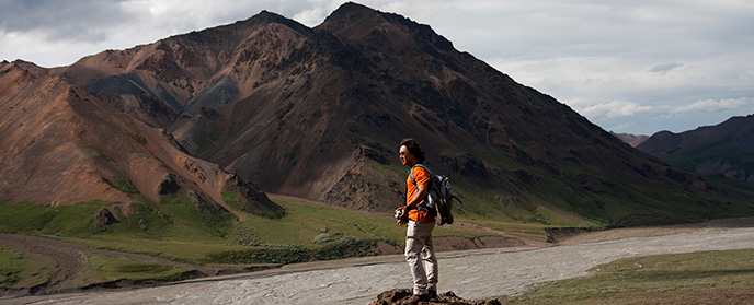 Hiker on a rocky outcrop, mountain and gravely river bar in distance