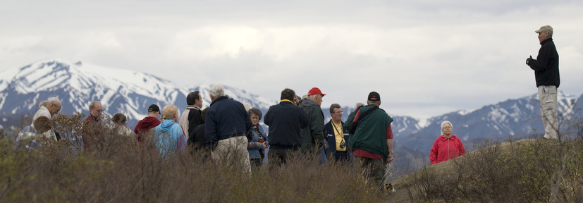 An Park Partner Interpreter speaks with a group of visitors to Denali, mountains are in the background.
